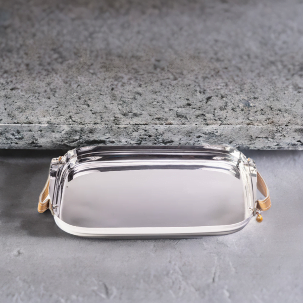Polished stainless steel tray with leather handles sitting on top of a marble surface.