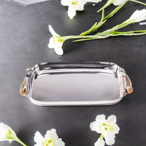 Polished stainless steel tray with leather handles on a black table with flowers on it.