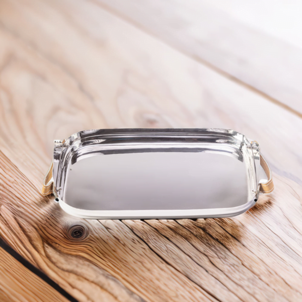 Polished stainless steel tray with leather handles sitting on top of a wooden table.