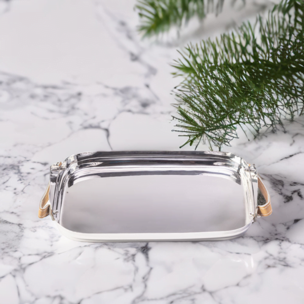 Polished stainless steel tray with leather handles on a marble table with a Christmas tree on it.