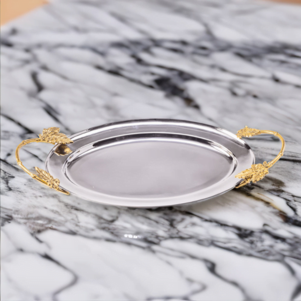 Polished stainless steel oval tray with gold handles on a marble surface.