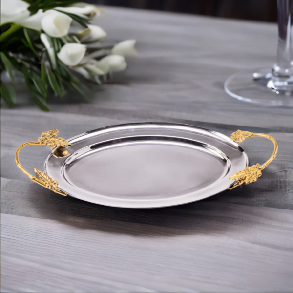 Polished stainless steel oval tray with gold handles on a wooden table.
