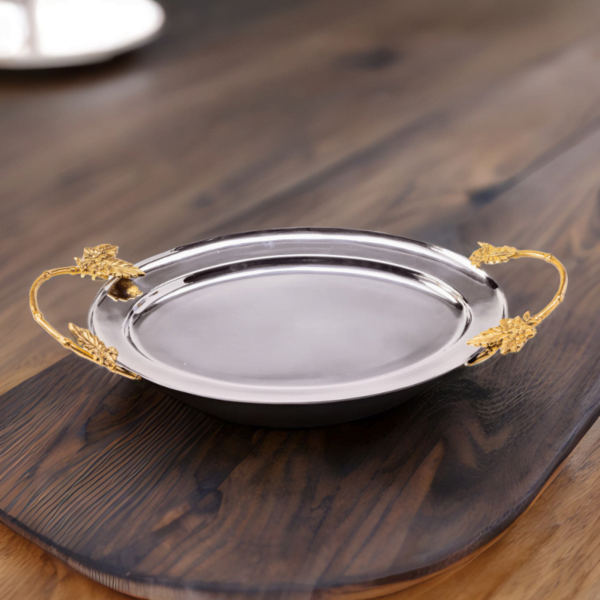 Polished stainless steel oval tray with gold handles on a wooden surface.