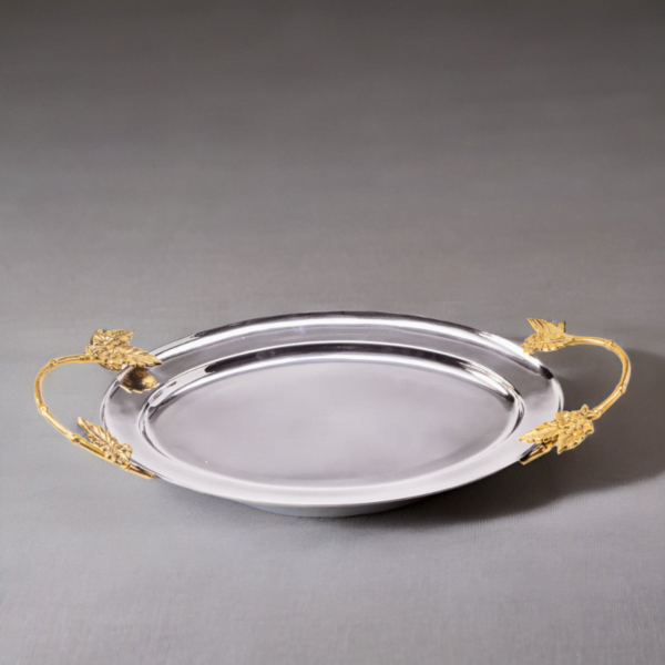 Polished stainless steel oval tray with gold handles on a grey surface.