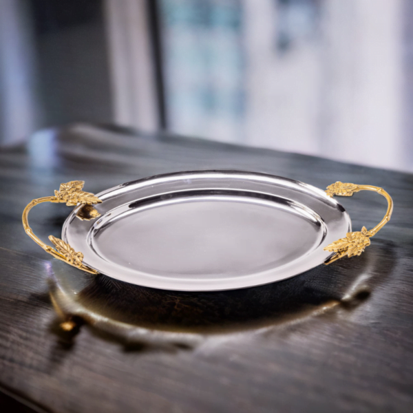 Polished stainless steel oval tray with gold handles on a dark wood table.