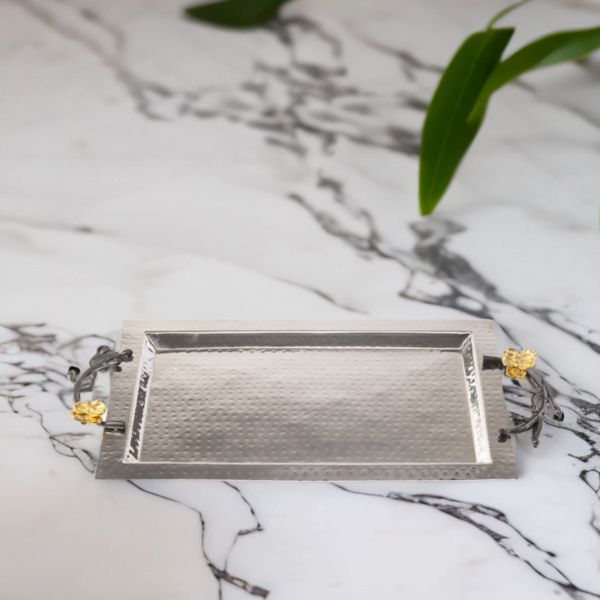 Rectangle hammered stainless steel serving tray with black handles and gold flowers sitting on top of a marble table.