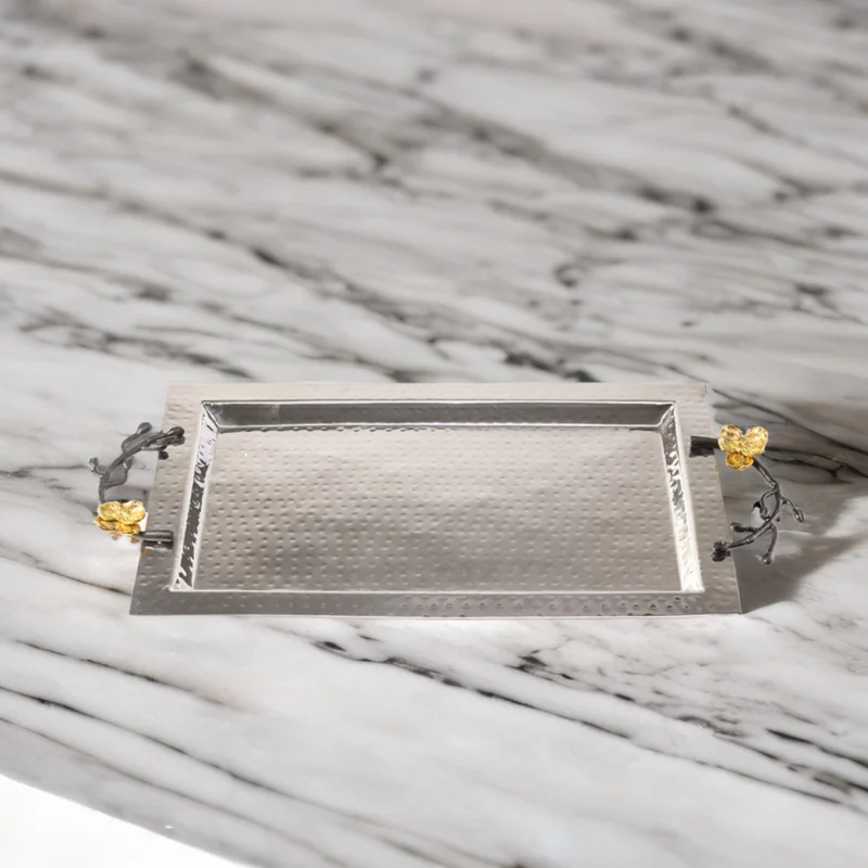Rectangle hammered stainless steel serving tray with black handles and gold flowers sitting on top of a marble counter.