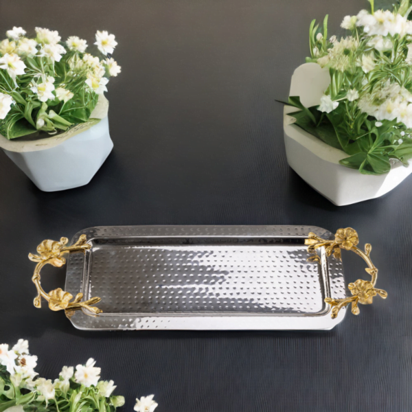 Rectangle hammered stainless steel serving tray adorned with gold handles on a table with 2 flower pots.