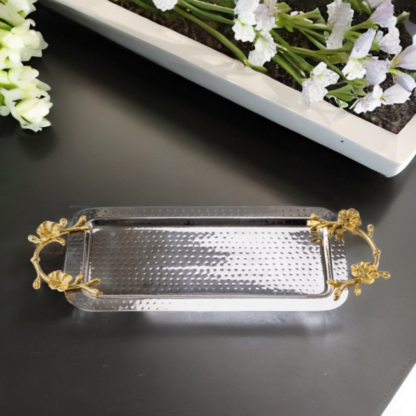Rectangle hammered stainless steel serving tray adorned with gold handles on a dark table.