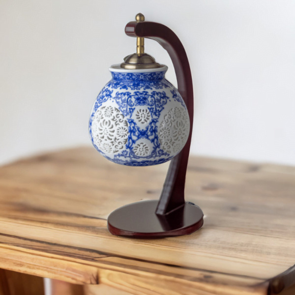 A wood lamp with a porcelain shade adorned with oriental blue and white flower styling on a desk.