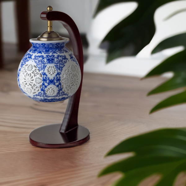 A wood lamp with a porcelain shade adorned with oriental blue and white flower styling on a wooden table.