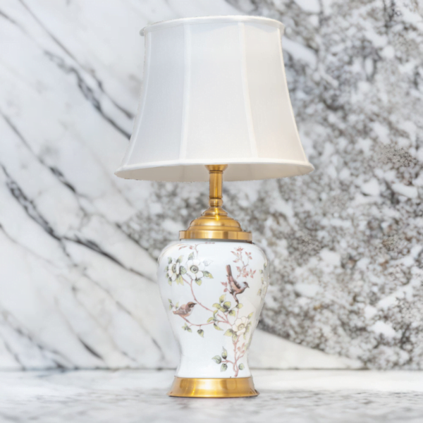A white porcelain lamp with matching white shade, gold accents and painted flowers and birds on a marble top.
