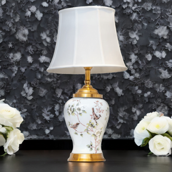A white ceramic lamp with matching white shade, gold accents and painted flowers and birds.