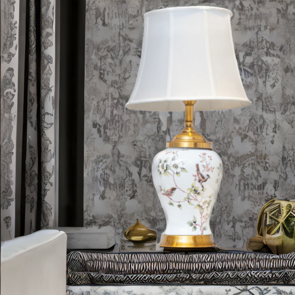 A white porcelain lamp with matching white shade, gold accents and painted flowers and birds.