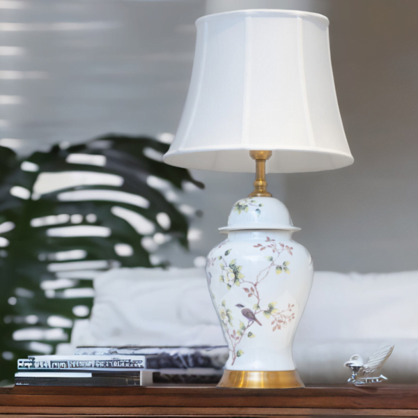 A white lamp with matching white shade, adorned with flowers and bird design, and gold accents.