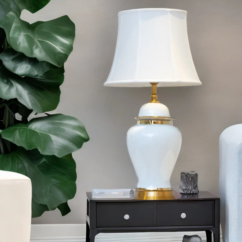 A white lamp with gold accents and matching white shade on a black wooden table.