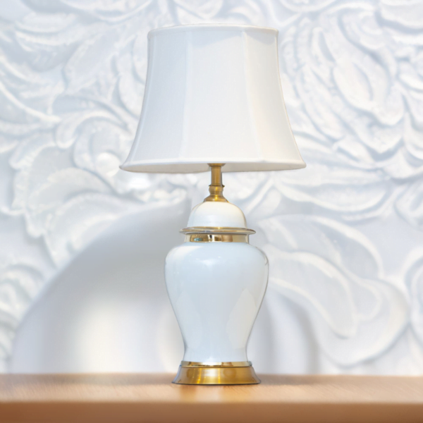 A white lamp with gold accents and matching white shade on a wooden table.
