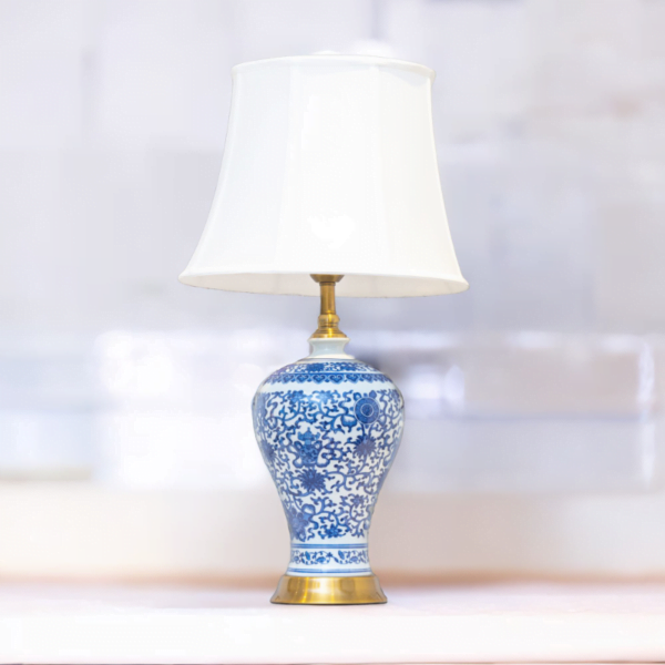 A blue and white lamp adorned with gold accents and stylish blue and white flower patterns and matching white shade.