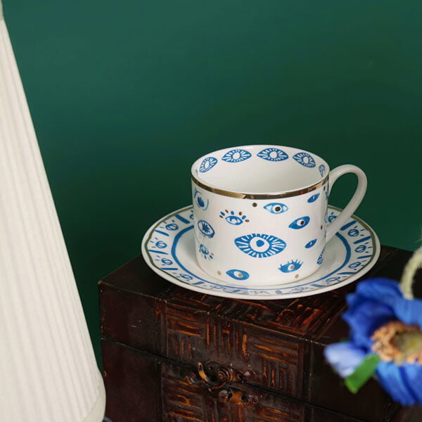porceline white tea cup with a saucer and evil eye prints all with gold edges