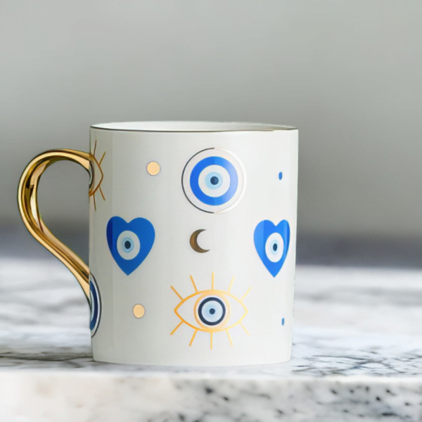 A white Azure Heart Mug with an evil eye on it on a marble top.
