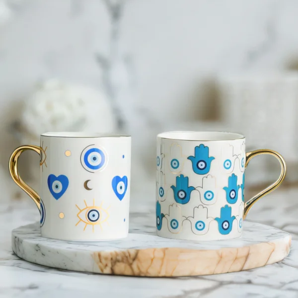 Azure Hamsa and Azure Evil Eye Mugs on marble top.