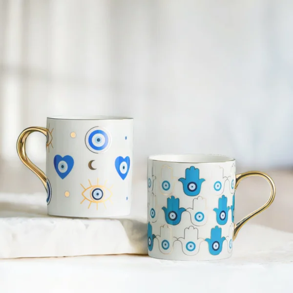 Azure Hamsa and Azure Evil Eye Mugs on marble top.