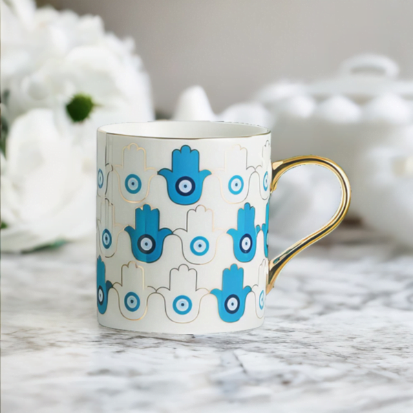 An Azure Hamsa Hand Mug, Blue and White with Gold accents on marble top.