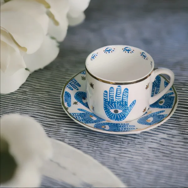 A Hamsa Blessings Set cup and saucer with a hand on it.
