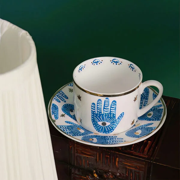 porceline white tea cup with a saucer and hamsa hand prints all with gold edges