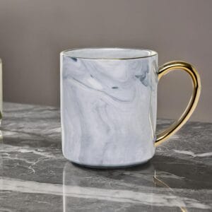 Ceramic mug with a granite look and a golden handle on a marble top.