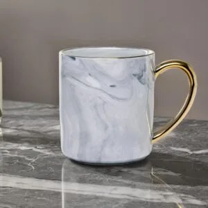 Ceramic mug with a granite look and a golden handle on a marble top.