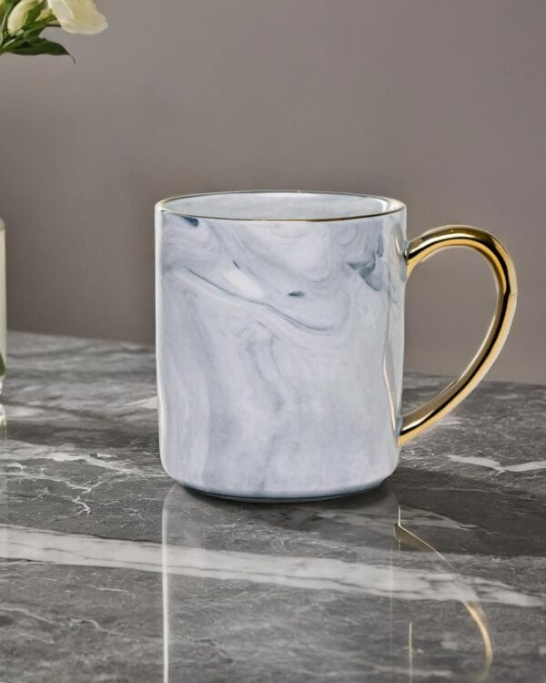 Ceramic mug with a granite look and a golden handle on a marble top.