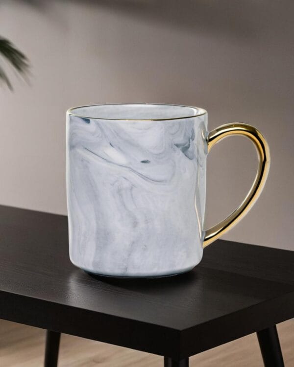 Ceramic mug with a granite look and a golden handle on a black wood table.