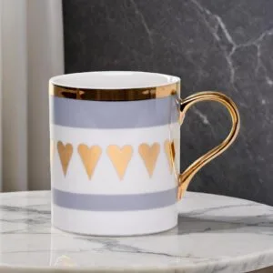 Ceramic mug adorned with golden hearts and a golden handle on a marble table.