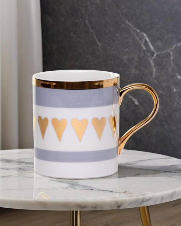 Ceramic mug adorned with golden hearts and a golden handle on a marble table.